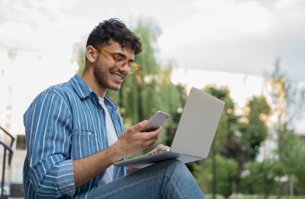 Junger Mann mit Laptop und Smartphone im Freien als Symbol für IT-Vertriebsberater Microsoft Cloud